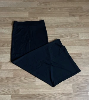 Svart långkjol i bomull - En stilren svart långkjol i mjukt bomullsmaterial. Kjolen har en rak och enkel design utan synliga detaljer eller mönster, vilket gör den lätt att matcha med olika toppar. Perfekt för dig som gillar minimalistisk stil och vill ha en bekväm kjol.