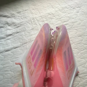 Lamine yamal retro limited edition  - Säljer ett par Adidas f50 fotbollsskor i en snygg rosa och vit färgkombination med lila och guldiga detaljer. Skorna har en strömlinjeformad design utan snörning, genomskinlig sula med dobbar och är tillverkade i syntetmaterial för lätt känsla på planen. Priset kan diskuteras 🤗