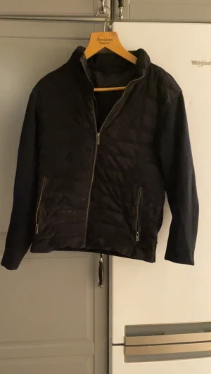 Svart mocka jacka från Massimo Dutti - Svart mocka jacka från Massimo Dutti med stilren design. Jackan har två sidofickor med dragkedja, hel dragkedja framtill och quiltade detaljer på framsidann. Materialet är syntet och mocka, vilket ger en schysst kontrast mellan kropp och ärmar.