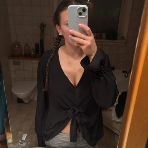 Svart blus med knyt framtill - Säljer en svart blus med v-ringning och knyt framtill. Blusen har långa ärmar med lätt puff och resår vid ärmslut. Perfekt för dig som vill ha en stilren men ändå trendig topp. Köpt från en lokal butik. One size men passar mig som har S, skulle säga den är i M kanske 💕 använd fåtal gånger!