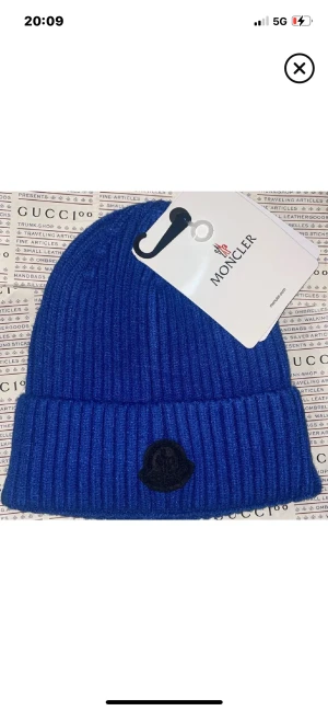 Blå ribbad mössa från Moncler - Snygg blå mössa från Moncler med ribbad struktur och uppvikt kant. Diskret svart Moncler-logga framtill. Perfekt för dig som vill ha en stilren och trendig accessoar till kalla dagar.