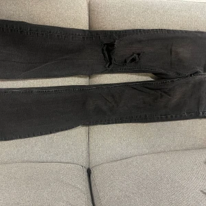 Svarta ripped jeans från Zara - Svarta jeans från Zara med slitna detaljer och hål på låret. (Egen gjorda hål) . Jeansen har råa, fransiga benslut. Materialet är jeans med dragkedja och knapp framtill. Färgen är washed out black. Använda men i bra skick