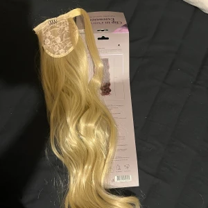Blond clip-in hästsvans - Helt nytt 60cm. Snygg clip-in ponytail i blond färg, gjord av högkvalitativa syntetfibrer. Ger snabbt extra längd och volym till håret. Lätt att fästa med osynlig klämma och passar perfekt för att skapa en fyllig hästsvans. Kan stylas med värme.