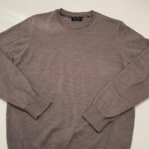 Sand tjocktröja - Säljer en stilren beige stickad tröja från Sand. Tröjan har rund halsringning, ribbade muddar och är tillverkad i mjuk ull. Perfekt för lager-på-lager och funkar året runt. Enkel att matcha med jeans eller chinos.