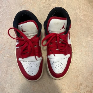 Nike Air Jordan 1 Low Chicago - Säljer ett par Nike Air Jordan 1 Low Chicago med klassisk röd, vit och svart färgkombination. Skorna har röd swoosh, röda snören och perforerad tå. Ovandelen är i skinn och de har en platt sula. Perfekta för dig som gillar ikoniska sneakers med streetstyle-vibe. Kan diskutera pris vid snabb köp.