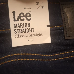 Lee Marion Straight mörkblå jeans - Mörkblå jeans från Lee, modell Marion Straight Classic Straight. Klassisk rak passform med snygga kontrastsömmar och Lee-logga på bakfickan. Tillverkade i slitstarkt denimtyg som ger en tidlös look.