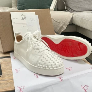 Christian Louboutin vita sneakers med nitar - Säljer ett par vita sneakers från Christian Louboutin i skinn med ikoniska röda mp sulor och coola nitar på tån. Nästan helt nya utan nån användning 