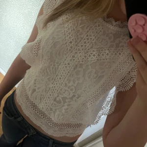 Vit spetsblus - Superfin vit blus i spets med vackra broderade detaljer och korta ärmar. Blusen har en croppad passform och rund halsringning med dekorativ kant.