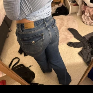 90s blå bootcut jeans - Säljer ett par klassiska 90s bootcut jeans i blå denim. Jeansen har bootcut-ben, fem fickor och normal midja. k. Perfekta för dig som gillar en tidlös och avslappnad look.