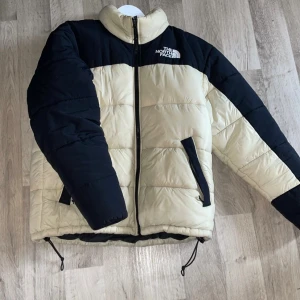 The North Face pufferjacket - Säljer en snygg pufferjacka från The North Face i beige och svart. Jackan har hög krage, dragkedja framtill, två fickor med dragkedja och justerbar dragsko nedtill. Perfekt för kalla dagar och riktigt skön att bära.  Jackan är i mycket bra skick. Tveka inte på att höra av dig vid intresse ‼️