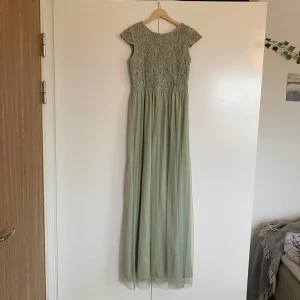 Ljusgrön långklänning från Bubbleroom - Supersnygg ljusgrön långklänning från Bubbleroom med spetsdetaljer upptill och v-ringning i ryggen. Klänningen har korta ärmar och ett flowy, tunnt tyll-tyg i kjolen.