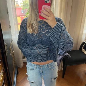 Blå stickad croppad tröja - Säljer en blå stickad tröja med coolt hålmönster och croppad passform. Tröjan har långärmade ärmar och breda ribbade muddar vid ärmslut och nederkant. Perfekt för dig som gillar en chill och trendig look.