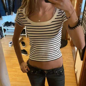 Randig topp från Gina Tricot - Säljer en vit och svart randig topp från Gina Tricot. Toppen har rundad halsringning, korta ärmar och är figurnära i passformen. Perfekt för dig som gillar enkel och stilren design med en fräsch vibe. Materialet är mjuk bomull som känns skönt mot huden. Storleken är liten så motsvarar xs-S 