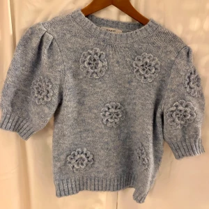Ljusblå stickad tröja med blommor MAPP - Superfin ljusblå stickad tröja från MAPP jeans med korta puffärmar och virkade blommor som dekoration. Tröjan har rund halsringning och ribbade muddar. Oanvänd köpt för två månader sedan nypris 599 kr 