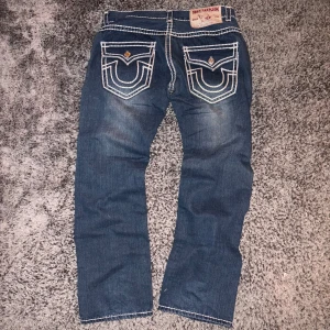 True Religion jeans med vita sömmar - Säljer ett par blå jeans från True Religion Jag köpte i japan i modellen JOEY SUPER T med ikoniska vita sömmar och broderade fickor bak. Jeansen har baggy passform, raka ben och klassisk femficksdesign med detaljerade nitar och logga. Materialet är slitstark denim i bomull. Kan fraktas eller mötas i linköping🌟