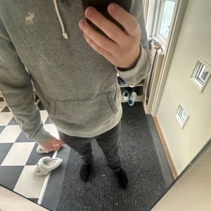 Grå hoodie Abercrombie & Fitch M - Säljer en grå hoodie från Abercrombie & Fitch i storlek M. Tröjan har huva med snörning, magficka och ett litet broderat älg-logo på bröstet. Mjuk insida och långärmad, perfekt för chill dagar. Passformen är normal och materialet känns som bomull och polyester.