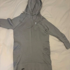 Grå hoodie från Kevin Levrone S - Snygg grå hoodie från Kevin Levrone Signature Series i storlek S. Tröjan har huva med snörning, långärmade ärmar och ett coolt strukturerat mönster. Märket syns både på bröstet och med metallbricka. Perfekt för gymmet eller chill. Endast använd en gång så i super bra skick! Stretchigt och skönt material!