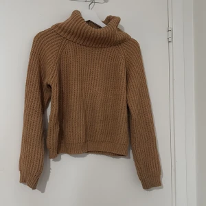 Beige stickad polotröja - Mysig beige stickad polotröja med grov ribbstickning och hög krage. Tröjan har lång ärm och avslappnad passform, perfekt för kyliga dagar. Enkel att matcha med jeans eller kjol för en chill look.