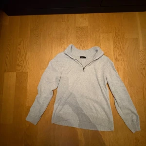 Ljusgrå stickad tröja half zip - Superskön ljusgrå stickad tröja från LMTD i storlek S. Tröjan har en ribbad krage med half zip-dragkedja och långa ärmar. Perfekt för dig som gillar enkel och clean stil med lite sportig touch. Ribbstickade muddar vid ärmslut och nederkant.