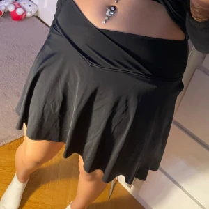 Svart tennis kjol - Supersnygg svart kjol i stretchigt tyg med V-formad midja – sitter jättefint på och ger en smickrande siluett! Bekväm, lätt och perfekt för både vardag och fest ✨ Storlek: M (stretchig) Aldrig använd 🖤 Passar perfekt till crop top, skjorta eller hoodie!