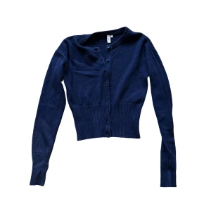 Marinblå kofta - Nelly - Snygg marinblå kofta från Nelly med ribbad midja och långa ärmar. Koftan har rund halsringning och knappar hela vägen framtill. Perfekt att styla med jeans eller kjol för en chill look.