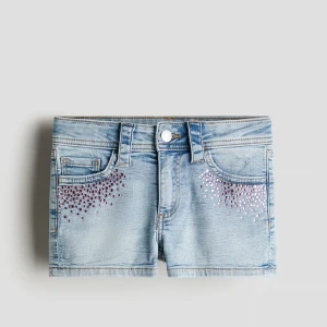 Ljusblå jeansshorts med rosa paljetter - Snygga ljusblå jeansshorts med rosa paljetter på framfickorna. Klassisk femficksmodell med knapp och dragkedja framtill. Shortsen har bälteshällor och är tillverkade i mjuk bomull. Perfekt för dig som vill ha lite extra bling på sommaren !!BARNSTORLEK 170 14+!! 