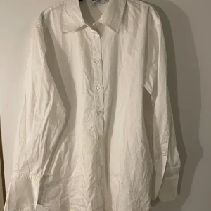 Vit skjorta från NA-KD, strl 36 - Klassisk vit skjorta från NA-KD med krage och knappar hela vägen framtill. Skjortan har lång ärm. Längre bak än fram