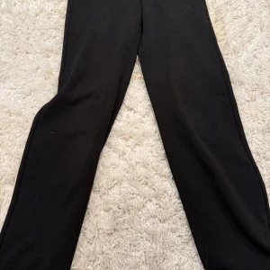 Svarta kostymbyxor från Vero Moda - Svarta byxor från Vero Moda med klassisk rak passform. Byxorna har en enkel och stilren design, perfekta att matcha med olika outfits. Materialet känns mjukt och bekvämt, vilket gör dem sköna att bära hela dagen.