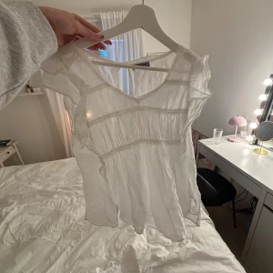 Vit blus med volang  - Säljer en söt vit blus från Hunkydory med volangdetaljer och lätt transparent tyg. Blusen har korta ärmar, v-ringad hals och flera dekorativa sömmar. Knappt använd!💞 