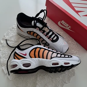 Nike Air Max Tailwind IV vit/orange - Nike Air Max Tailwind IV sneakers i vitt, orange och svart med rosa detaljer. Snygg retrodesign med synliga Air Max-enheter i sulan, svarta snören och meshpaneler för extra andningsförmåga. Perfekta för dig som gillar statement-sneakers med cool färgkombo.