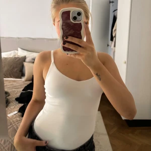 Vit body med smala axelband - Säljer en enkel och fräsch vit body med smala axelband och v-ringad hals. Toppen är tight och har en clean look som funkar till jeans eller kjol. Perfekt för dig som gillar minimalistisk stil och vill ha en basic topp i garderoben.