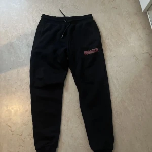 Svarta mjukisbyxor från Hoodrich - Svarta mjukisbyxor från Hoodrich med röd logotyp på vänster lår. Byxorna har snörning i midjan och ribbade muddar vid bensluten. Perfekta för chill eller streetwear och gjorda i mjukt material för extra komfort.
