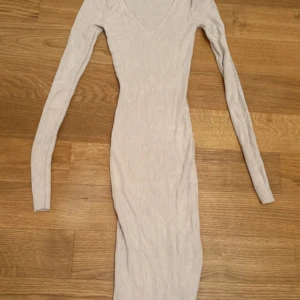 Beige ribbad långklänning från Amisu - Snygg beige långklänning från Amisu med ribbad struktur och v-ringad hals. Klänningen har lång ärm och är figurnära i modellen, perfekt för dig som gillar en slim passform. Materialet är mjukt och stretchigt, vilket gör den superbekväm att bära.