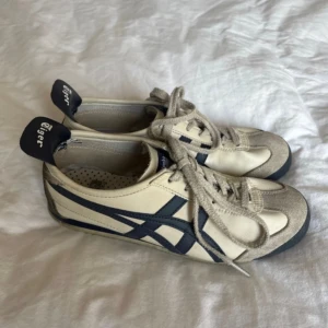Onitsuka Tiger  - Säljer ett par klassiska Onitsuka Tiger sneakers i vitt och mörkblått med snygga ränder på sidorna. Perfekt för hösten!! 