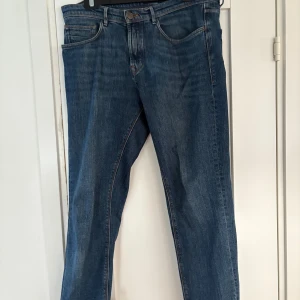 Blå jeans från Massimo Dutti, strl 40 - Snygga blå jeans från Massimo Dutti i klassisk femficksmodell. Jeansen har rak passform, normal midja och är tillverkade i slitstarkt denim med subtila tvättade detaljer. Perfekta för dig som gillar stilrena och tidlösa jeans.