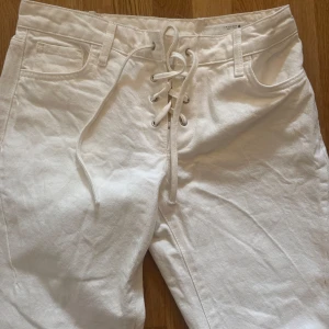 Vita jeansbyxor med snörning - Snygga vita jeansbyxor med cool snörning framtill i midjan. Byxorna har klassisk femficksdesign och raka ben. Materialet är stadigt och känns som bomull, perfekt för dig som vill sticka ut med en unik detalj på dina jeans. Jeansen är från Zara o används 1 gång 