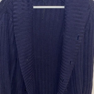Mörkblå ribbad kofta med knappar - Säljer en mörkblå, ribbstickad kofta med bred krage och dubbla rader svarta knappar framtill. Koftan har lång ärm och är gjord i ett mjukt, stickat material som passar perfekt till kyligare dagar.