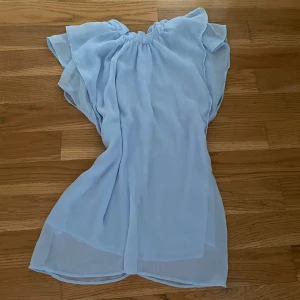 Ljusblå topp  - Superfin ljusblå blus i luftig chiffong med volangdetaljer vid axlarna och omlottkänsla. 