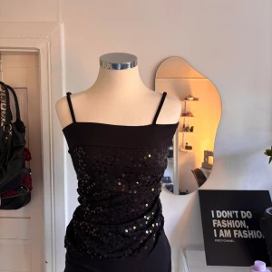 Svart paljettlinne vintage - Svart linnetopp  med smala axelband och glittriga paljetter framtill. Toppen har en rak halsringning och är figurnära i modellen. Köpt vintage 