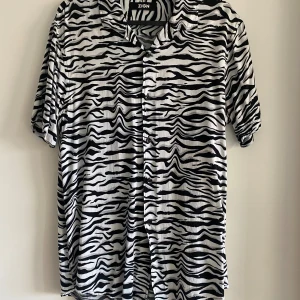 Zebra-mönstrad herrskjorta från Zign S - Säljer en kortärmad cool mönstrad herr t shirt/ skjorta från Zign med svartvitt zebramönster. Skjortan har krage, knappar framtill och är tillverkad i mjuk viskos som känns skön mot huden. Storlek S
