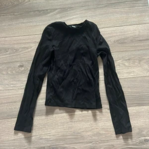 Svart långärmad tröja  - En basic svart ribbstickad långärmad tröja från Bik Bok i mjuk bomull. Enkel och stilren modell med rund halsringning och normal passform. Perfekt att matcha med jeans eller kjol för en clean look.