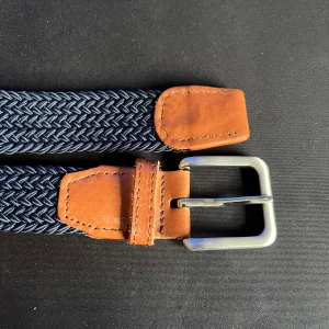 Mörkblå flätat bälte med skinn - Snyggt mörkblått flätat bälte med detaljer i brunt skinn och silvrigt spänne. Bältet har en stilren design med vävd struktur och klassiska skinnpartier vid spännet och ändarna. Perfekt accessoar för att lyfta din outfit.