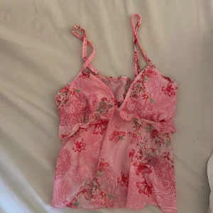 Rosa blommig linnetopp från SHEIN - Supersöt rosa linnetopp från SHEIN med blommigt mönster och volangdetalj under bysten. Tunn och flowy polyester med justerbara smala axelband och v-ringad hals. Perfekt för sommarens alla häng! 🌸