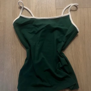 Bershka linne - Snygg grön linnetopp med tunna axelband och vita kontrastkanter. Enkel och stilren design som passar perfekt till jeans eller kjol. Mjuk och skön bomullskänsla, perfekt för varma dagar.