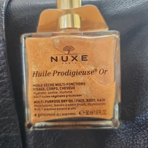 Nuxe Huile Prodigieuse Or torr olja 50 ml  - Glittrande multifunktionell torr olja för ansikte, kropp och hår från Nuxe. Kommer i en lyxig glasflaska med guldskimrande olja som ger huden en satinfinish och subtila gyllene toner. Innehåller 7 botaniska oljor och är vegansk.
