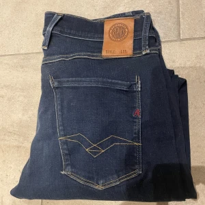 Replay Anbass jeans mörkblå, - Säljer ett par mörkblå Replay Anbass jeans med klassisk femficksdesign och snygga kontrastsömmar. Jeansen har raka ben och normal passform, tillverkade i mjukt jeansmaterial. Märkespatch bak i midjan och diskret logga på bakfickan.
