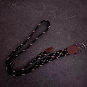 Svart flätat bälte med mönster - Säljer ett svart flätat bälte med snyggt mönster i beige och brunt. Bältet har detaljer i brunt skinn vid spännet och en silvrig metallspänne. Flätad design som ger en cool och unik look, perfekt för att lyfta din outfit.
