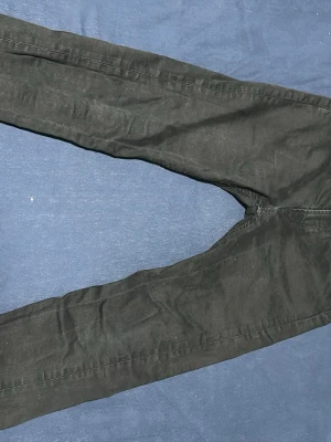 Svarta jeansbyxor från Dressmann - Svarta jeansbyxor från Dressmann med regular fit och klassisk femficksdesign. Byxorna har silverfärgade nitar och knapp, samt raka ben. Materialet är jeans och färgen är helsvart, vilket gör dem enkla att matcha med olika stilar.