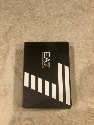 Emporio Armani EA7 svarta sneakers - Säljer ett par stilrena svarta EA7 Emporio Armani sneakers med meshpaneler och snygga detaljer i silver. Skorna har snörning, platt sula med räfflad undersida och logga på sidan. Perfekta för dig som gillar sportig och modern design. Priset går att diskutera.