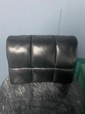 Svart quiltad axelväska från Stand Studio - Säljer en svart axelväska från Stand Studio med quiltad design i stora rutor. Väskan är tillverkad i mjukt skinn och har en magnetisk knappstängning. Perfekt storlek för att få plats med allt du behöver och har en lyxig vibe som sticker ut.